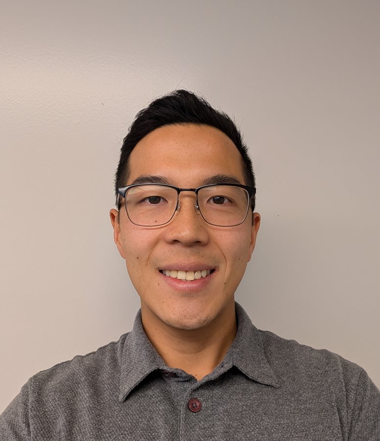 The image shows a person wearing a grey polo shirt, with their hair styled in a dark, neat haircut. AI-generated content may be incorrect.
